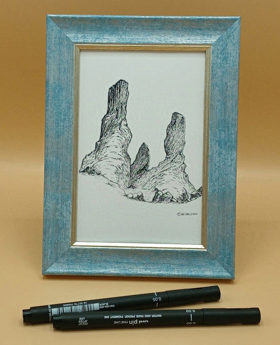 Framed black and white drawing of a natural landscape with two pens on a beige background