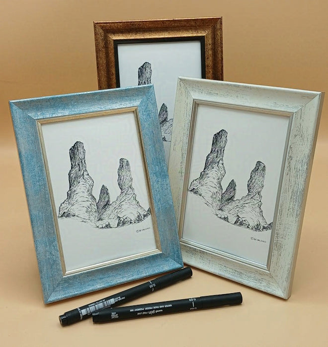 Three framed artworks of rock formations on a beige surface with two black markers.