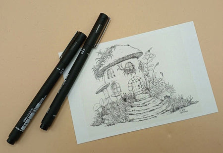 Two black markers on a beige surface with a drawing of a fairy house with a mushroom shaped roof