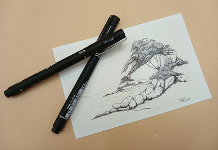 Two black markers on a piece of paper with an ink sketch of trees on rocky islands