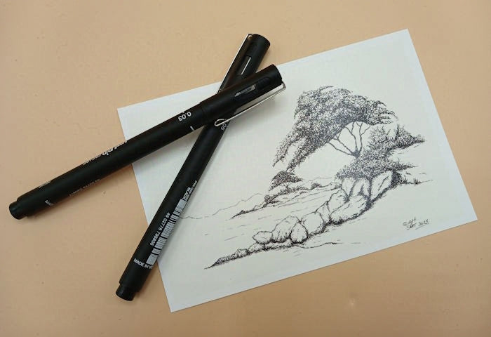 Two black markers on a piece of paper with an ink sketch of trees on rocky islands