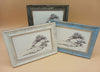 Three framed black and white landscape drawings featuring on a beige background featuring trees on rocky islands