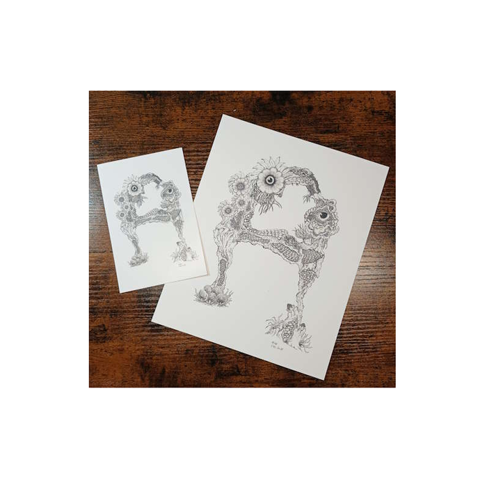 Two paper prints with intricate black and white design of the letter "A" on a wooden surface